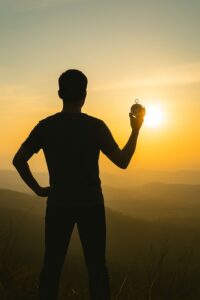 Siluet seseorang berdiri di puncak bukit menikmati matahari terbit sebagai simbol awal baru dan harapan.